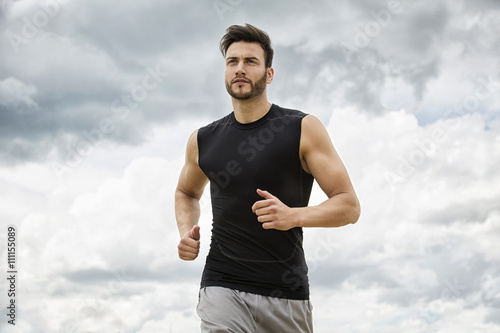 Muscular man jogging outdoors, dramatic sky backdrop photo