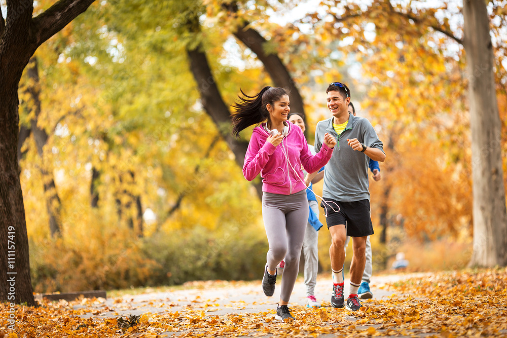 A lively group of young friends enjoys a refreshing jog in the park during the vibrant autumn season, relishing the camaraderie and the crisp, cool air. A lively group of young friends enjoys a refreshing jog in the park during the vibrant autumn season, relishing the camaraderie and the crisp, cool air.