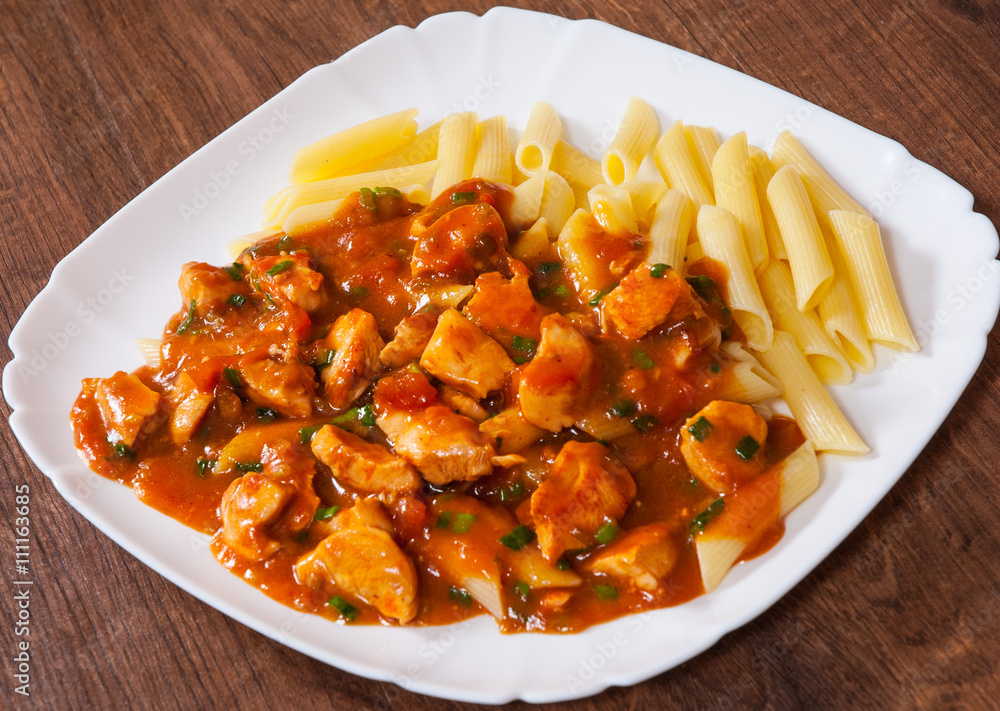 chicken breast in tomato sauce with penne pasta in a plate on wooden table chicken breast in tomato sauce with penne pasta in a plate on wooden table