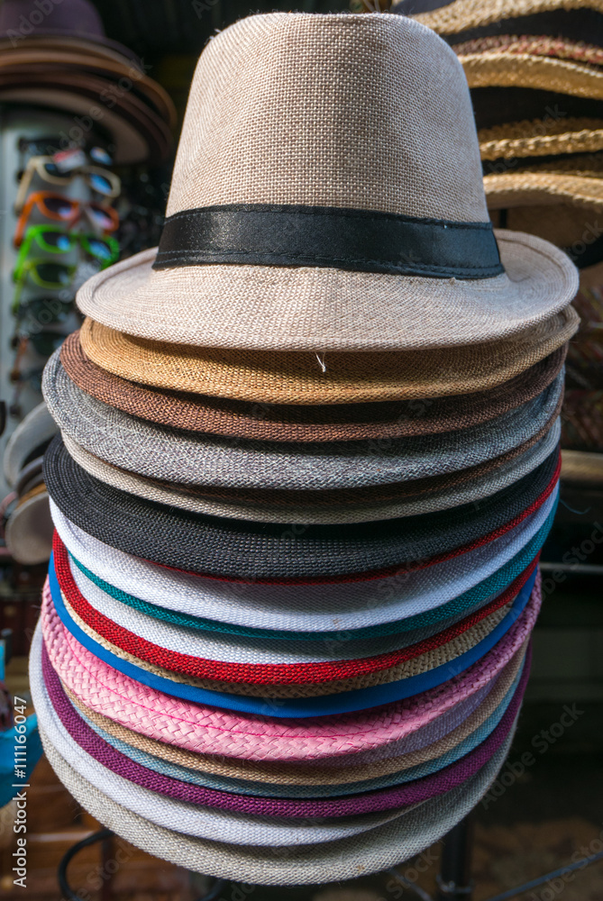 Stacked white and colored Balinese tourist hats laying market stall of Ubud. Bali, Indonesia (Selective focus)