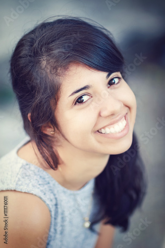Portrait of beautiful Hispanic latino white girl woman with brown eyes, long dark curly wavy hair in gray dress sitting in park outside smiling laughing looking in camera, lifestyle portrait concept
