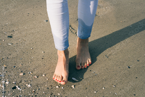 Bare female feet walking on wet sand at beach