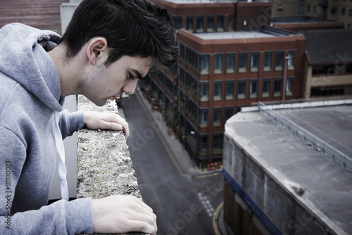Depressed Young Man Contemplating Suicide On Top Of Tall Buildin