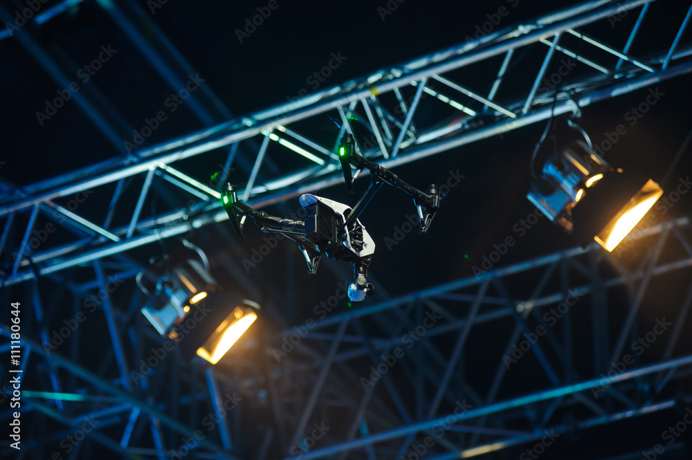 Flying drone above the stage/White quadrocopter drone with camera flies against stage constructions 