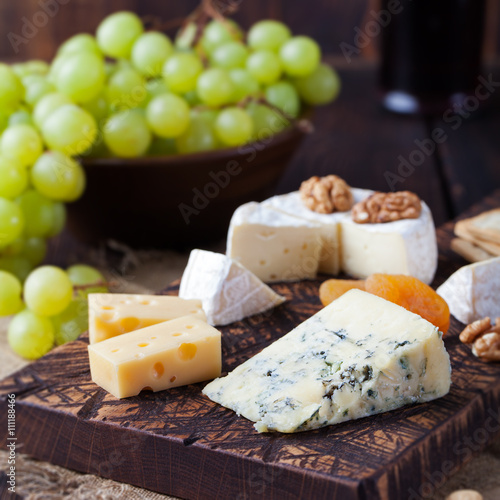 Assortment of cheese with honey, nuts and grape on a rustic cutting board