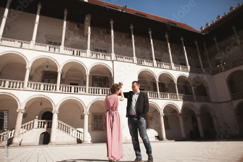 Beautiful couple, man, girl with long pink dress posing in old castle near columns. Krakow Vavel