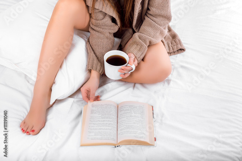 Attractive woman with a cup of coffee and book on the bed