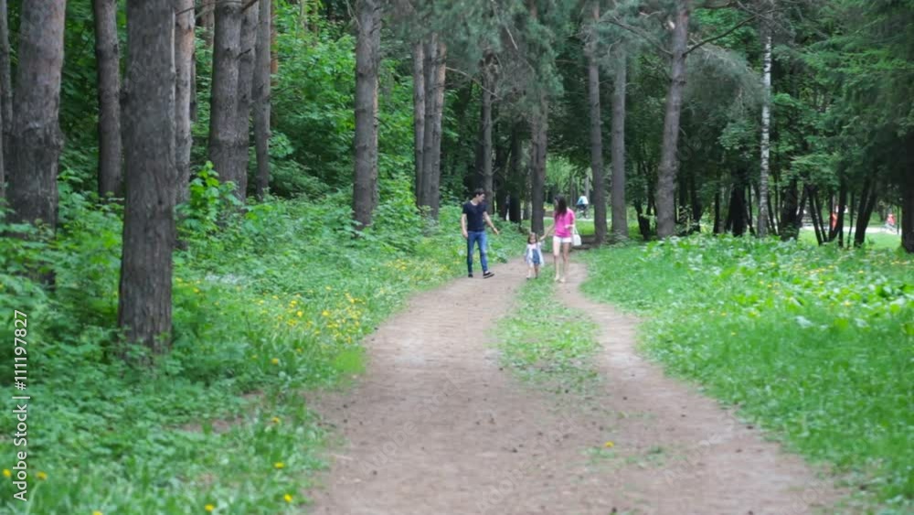 Mom and young daughter and dad, a young family on a walk in the park in summer Mom and young daughter and dad, a young family on a walk in the park in summer