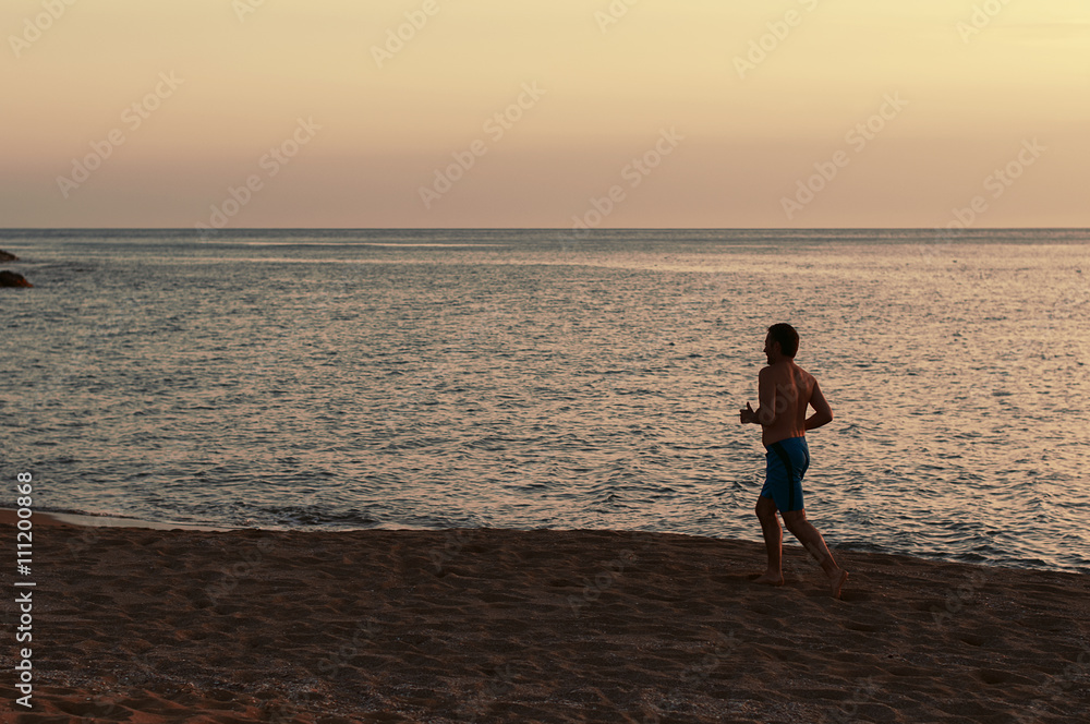 Handsome fit man running on the sunset beach