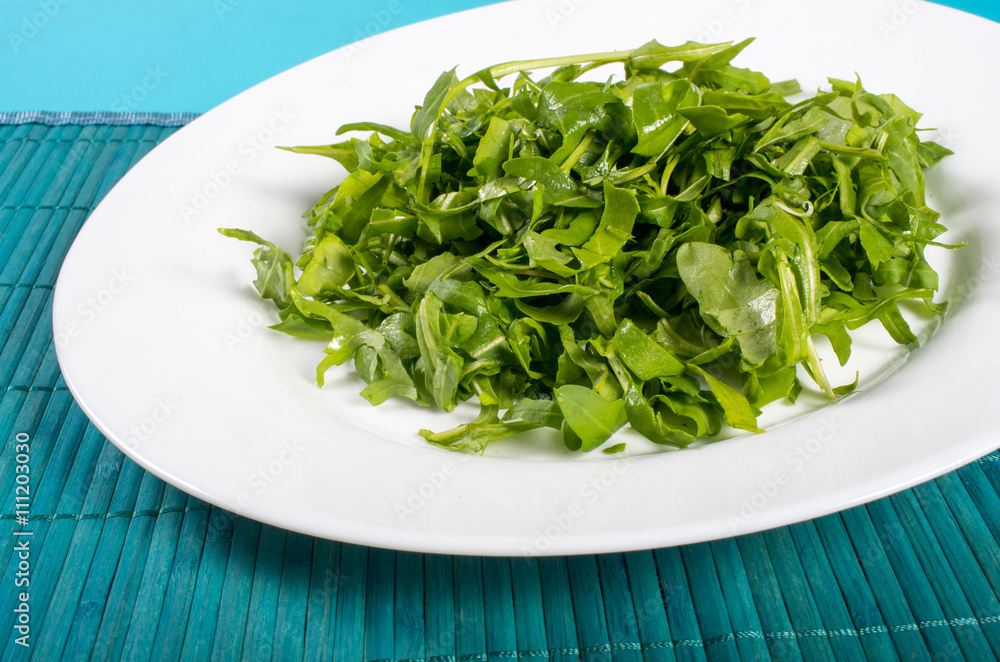 A white plate with a salad of arugula on a blue-green place mat. A white plate with a salad of arugula on a blue-green place mat.