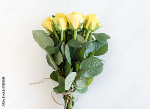High angle view of bouquet of yellow roses with green leaves and stems tied with brown string on white table