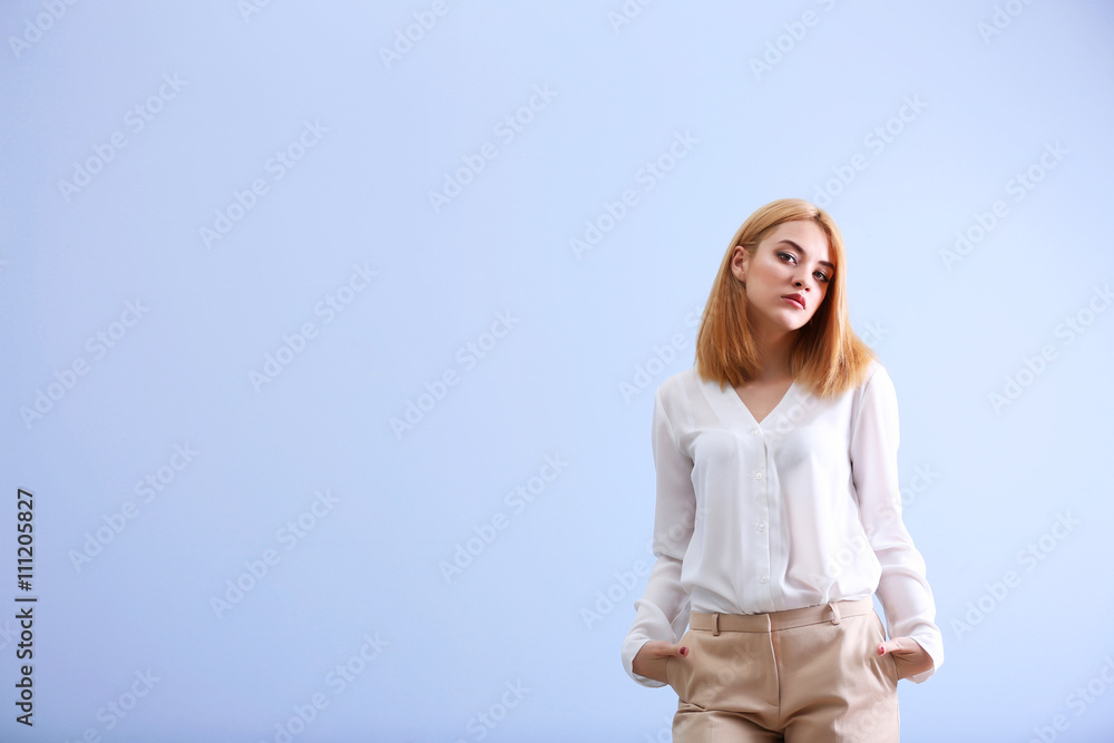 Beautiful blonde young woman in white shirt and beige pants on blue wall background Beautiful blonde young woman in white shirt and beige pants on blue wall background