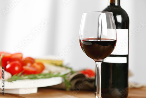 Glass and bottle of red wine with food on blurred background