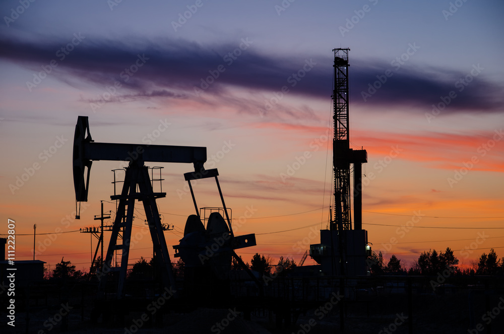 Pump jack and derrick silhouette during sunset on the oilfield. Oil and gas concept. 