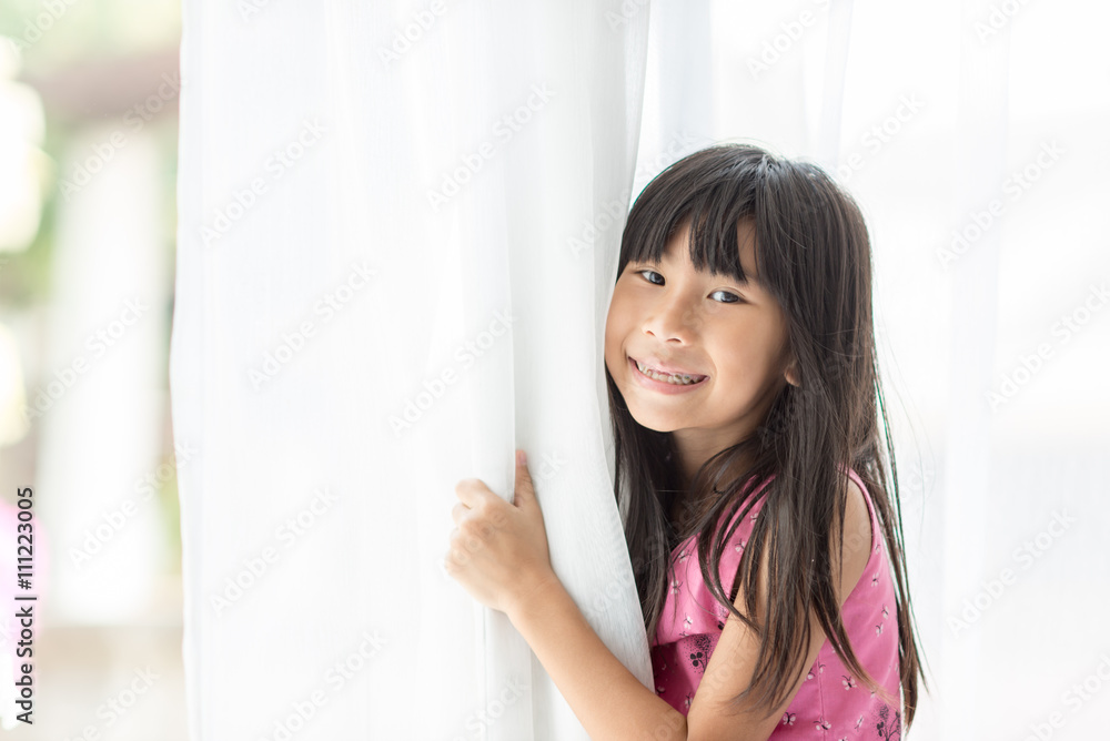 Happy Asian girl holding white curtain at home with copy space. Happy Asian girl holding white curtain at home with copy space.