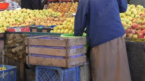 Fruit seller wearing traditional Islamic robe djellaba is washing apples at his stall at Moroccan market 