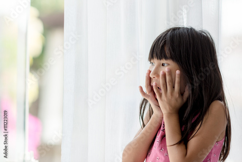 Happy Asian girl looking out of window and surprising