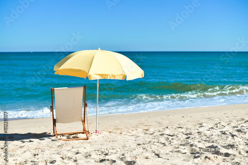 Yellow umbrella and wooden chair on Atlantic sandy beach