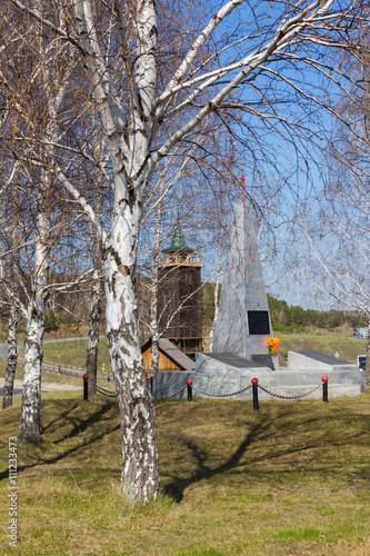 Old wooden fire tower on the background of the monument to the fallen soldiers. Sinyachikha, Ural, Russia. photo