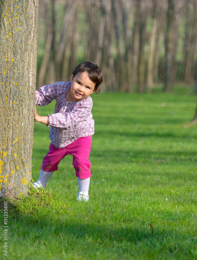 Little girl hiding behind a tree in a forest Little girl hiding behind a tree in a forest