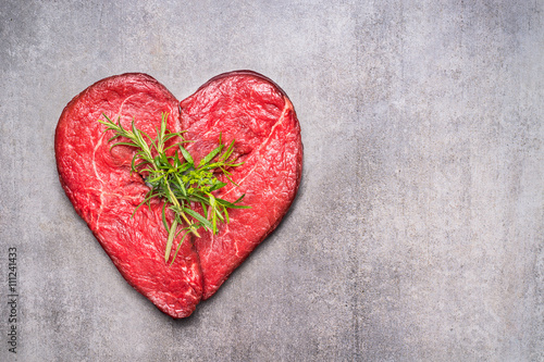 Heart shape raw meat with herbs and text on gray concrete background , top view, horizontal photo