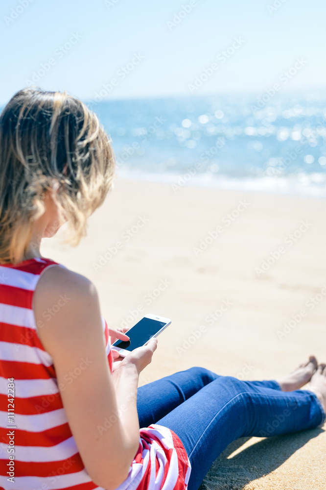 Female holding mobile phone on beach sandy background, Back view