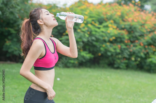 young attractive woman drinking water from plastic bottle in the park