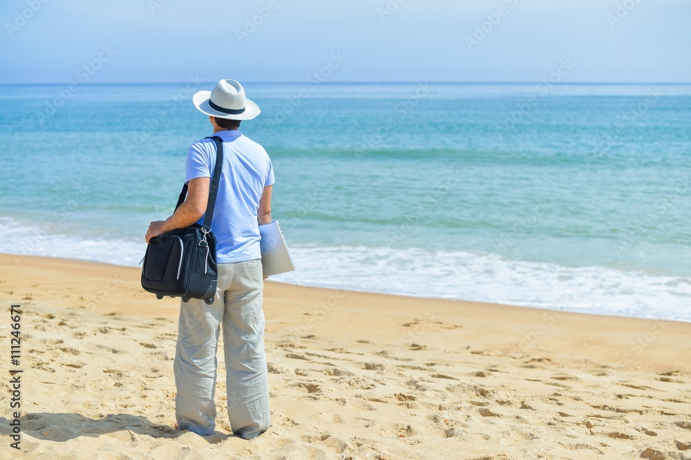 Businessman holding laptop suitcase standing on beach outside. background outdoors