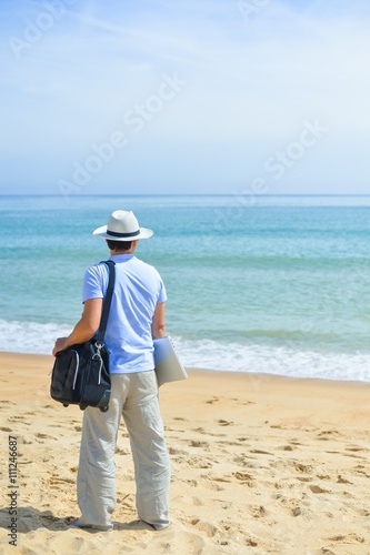 Back view on man with laptop on the beach sunny blue sky background