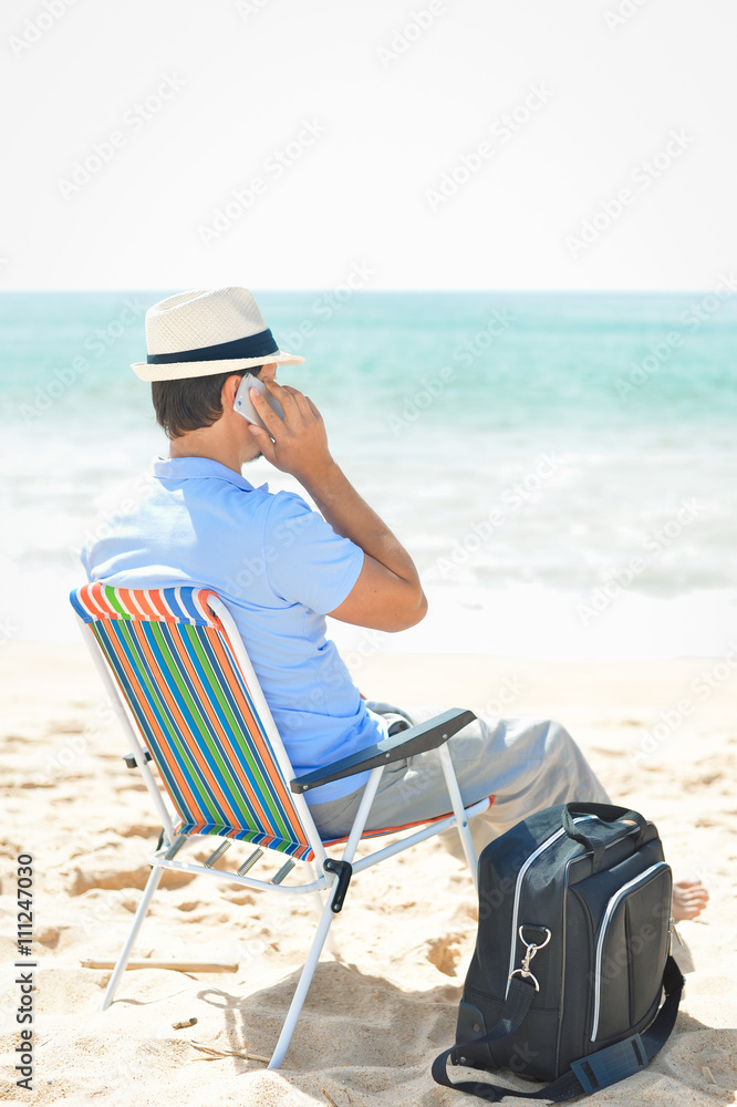 Man chilling on the beach talking on smartphone. Back side view of guy enjoying outdoors background