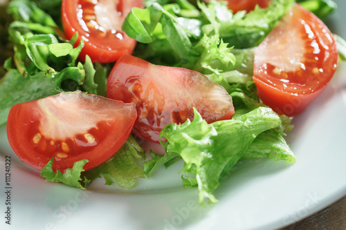 closeup photo of fresh summer salad with tomatoes, rucola and frillis leaves in plate on wood table, shallow focus