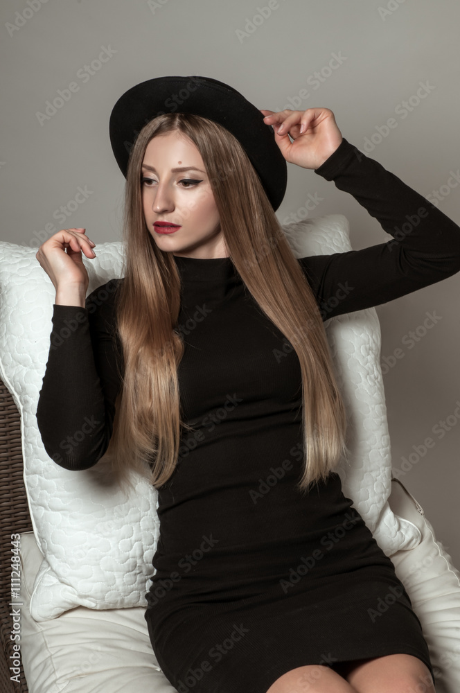Woman with long straight blond hair in a black hat and dress sitting on a chair. Woman with long straight blond hair in a black hat and dress sitting on a chair.