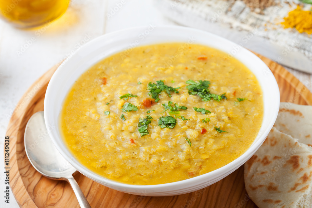 Lentil soup with pita bread in a ceramic white bowl on a wooden background.