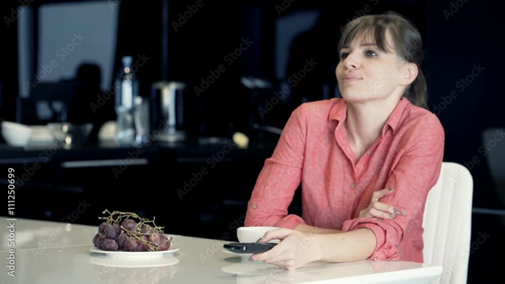 Young, happy woman watching TV sitting by table in kitchen at home
Young, happy woman watching TV sitting by table in kitchen at home