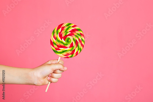 Colorful lollipop in child hand on pink background. Copy space.
