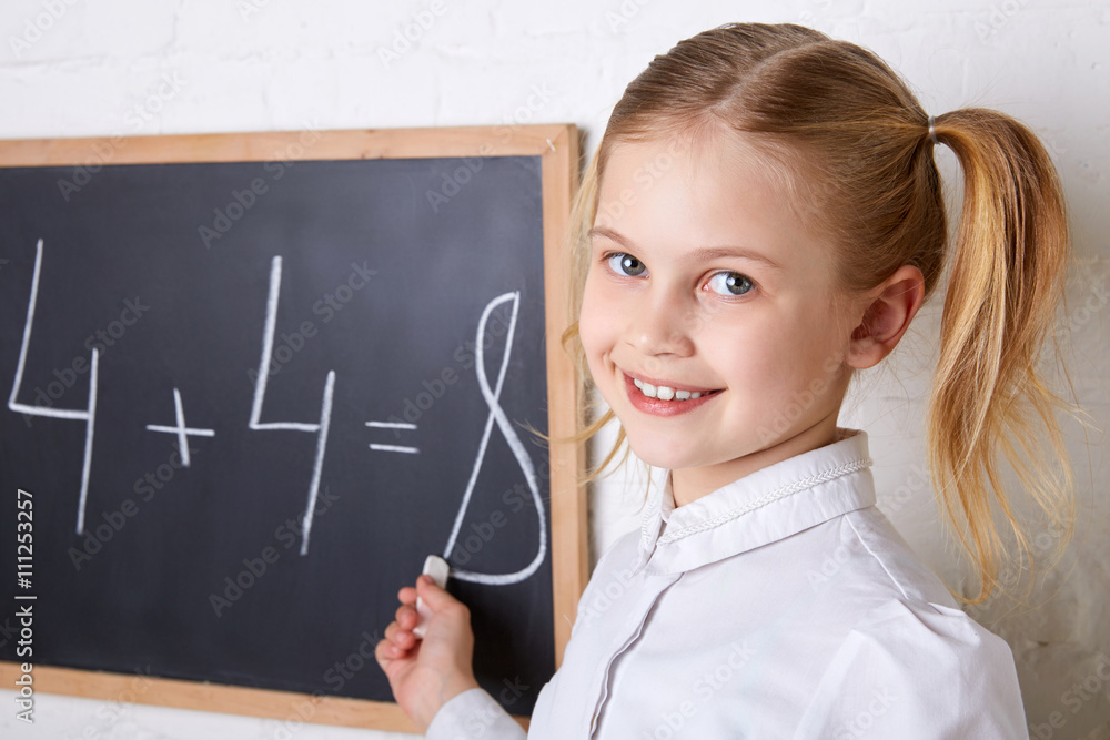 Pretty schoolgirl standing near blackboard with piece of chalk and smiling Pretty schoolgirl standing near blackboard with piece of chalk and smiling