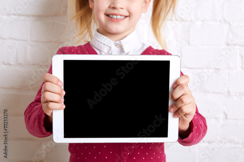 Pretty little girl holding a tablet on light background. Close up. Copy space.
