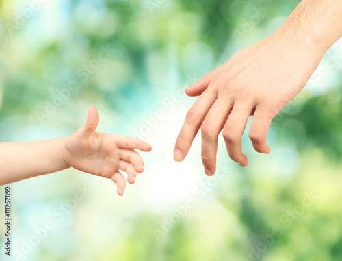 Child and dad  hands on green nature background. Concept of taking care, protection, helping and assistance © Africa Studio