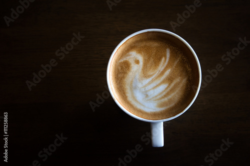 Cup of latte art coffee with froth shape bird and wooden backgro