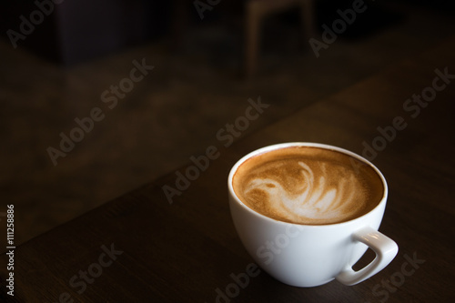 Cup of latte art coffee with froth shape bird and wooden backgro