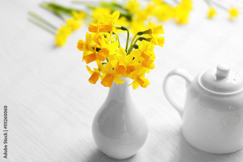 Fresh narcissus flowers and teapot on wooden background
