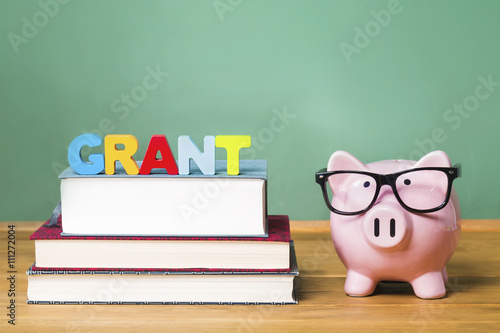 Education grant theme with pink piggy bank on top of books with chalkboard in the background