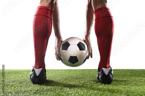 legs of football player in red socks and black shoes holding the ball in his hands placing free kick