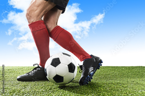 legs of football player in red socks and black shoes running and dribbling with ball playing outdoors
