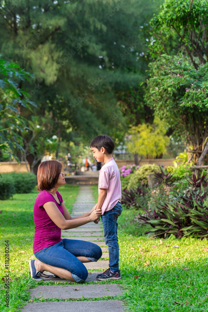 Fototapeta premium Mother sitting at park holding hands and teaching her son