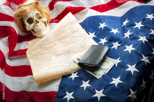 A human skull wearing a ginger wig on top of the US constitution and the upside down american flag symbolizing the danger that demagoguery, racism, manipulation and hatred can bring to freedom photo