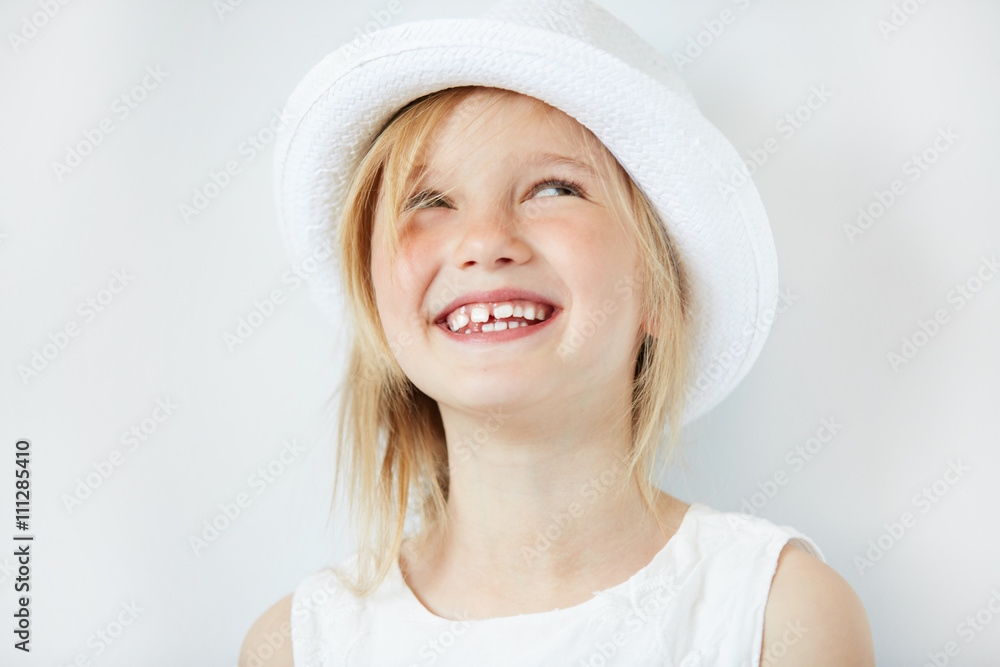 Close up portrait of adorable blonde little girl wearing white hat, laughing and having fun indoor. Cute 5-year old female smiling and showing her teeth. Isolated portrait of beautiful Caucasian child Close up portrait of adorable blonde little girl wearing white hat, laughing and having fun indoor. Cute 5-year old female smiling and showing her teeth. Isolated portrait of beautiful Caucasian child
