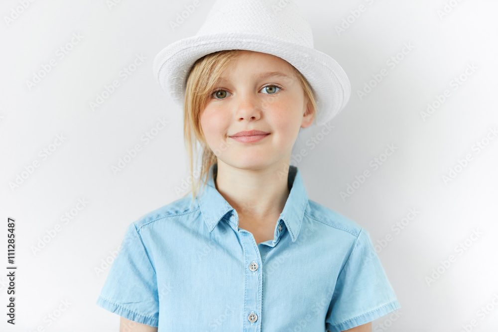 Close up portrait of adorable blonde little girl wearing white hat and blue shirt smiling and having fun indoor. Cute preschool female looking at the camera. Isolated shot of beautiful Caucasian child Close up portrait of adorable blonde little girl wearing white hat and blue shirt smiling and having fun indoor. Cute preschool female looking at the camera. Isolated shot of beautiful Caucasian child