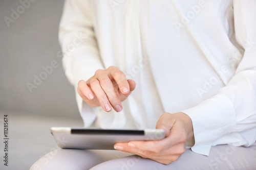 Cropped view of female using tablet computer with touch screen, messaging via social networks, reading news or watching pictures or videos. Close up shot of woman's hands holding electronic gadget