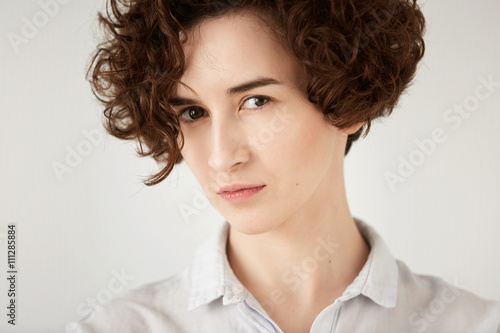 Close up studio portrait of young displeased or angry woman looking in annoyance. Isolated headshot of irritated girl with short curly red hair white hipster shirt. Human face expressions and emotions